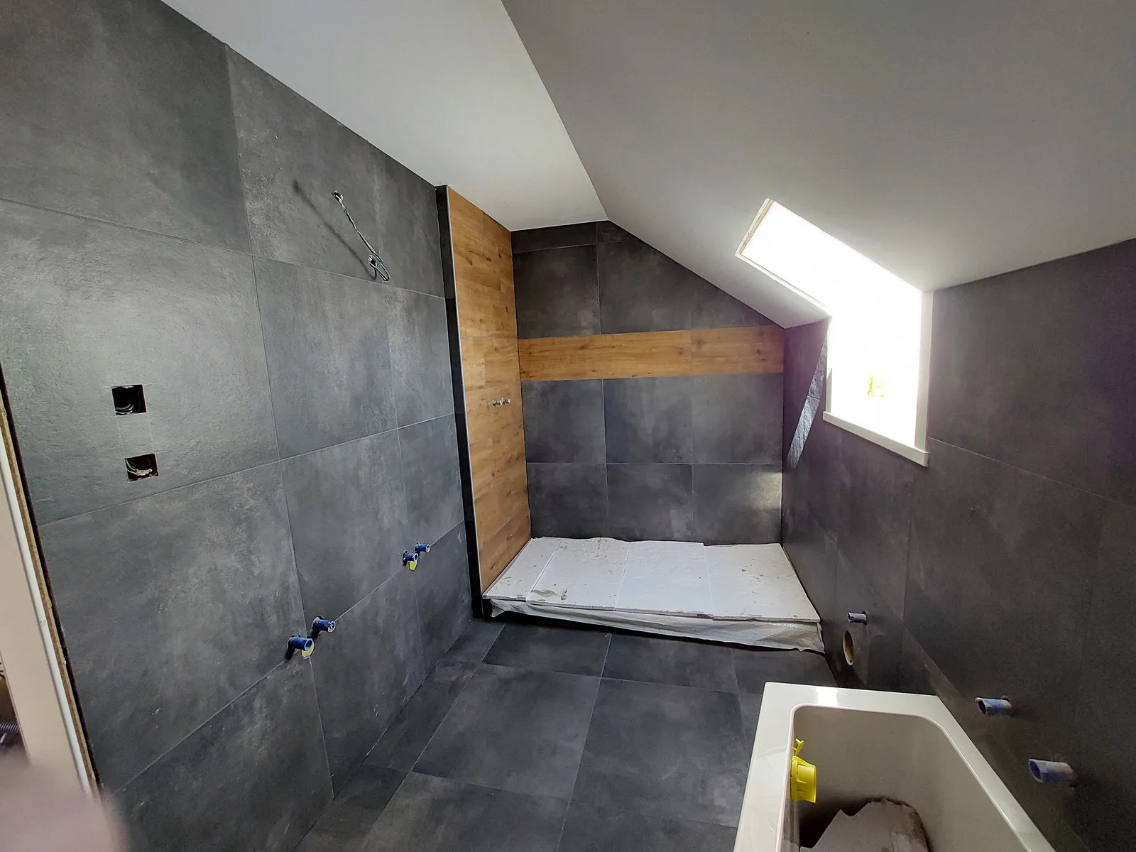 Salle de bains sous combles : murs et sol en grès cérame anthracite 60×60, niche habillée de carrelage effet chêne